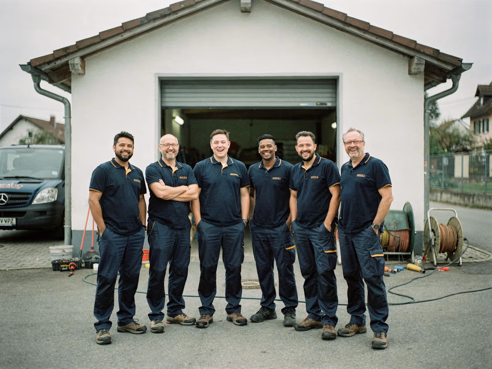 Team von fünf bis sechs Elektrikern aus Ulm vor einer kleinen weiß verputzten Werkstatt